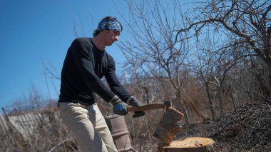 Genç bir öğrenci odun kırmayı öğreniyor. Kış için odun topluyorum. Adamın biri baltayla odun kesiyor. Bandana ve siyah bir gömlek giyiyor. Sahne açık havada, gökyüzü mavi.