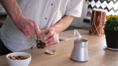 Şık bir mutfakta kahve yapan bir adamın yakın çekimi. Cam kavanozdan bir kaşık dolusu mis kokulu kahve çıkarıyor. Türkçe kahve yapmak. Güzel bir sabah. 
