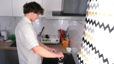 Yakışıklı bir adam mutfakta kahve yapıyor. Fırının üzerindeki Türk 'ün kahvesini kaşıkla karıştırıyor. Bekar bir adamın sabahı. Bekar adam kendi kahvaltısını hazırlar..