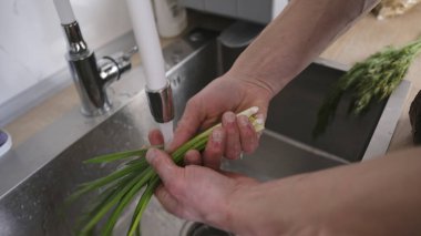 Vejetaryen bir adam mutfak lavabosunda mercanları yıkıyor, yakın plan. Adam kendine taze doğal sebzelerden oluşan bir öğle yemeği pişiriyor. Uygun beslenme