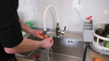 Bir adam musluğun altında temiz suyla taze havuç yıkıyor. Aşçı öğle yemeği hazırlıyor. Sebze yıkıyorum. Şık bir mutfak. Lavabo gümüş, musluğu var.