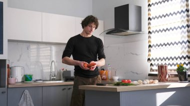 Şirin, uzun boylu, beyaz adam mutfakta elinde havuçlarla dikiliyor. Bir adam lezzetli bir öğle yemeği pişirecek. Mutfak temiz ve iyi döşenmiş. Adam görevine odaklanmış durumda ve bu sahne bir sakinlik hissi veriyor..