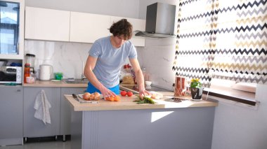 Güzel genç bir öğrenci kız arkadaşı için öğle yemeği hazırlar. Adam mutfakta duruyor, dikkatlice sebzelere bakıyor. Mutfak temiz ve bakımlı. Bir adam kesme tahtasıyla sebze kesiyor.