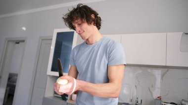 Yakışıklı romantik bir eşcinsel mutfakta dans ederken beyaz soğan kesiyor. Sebze yemeği pişiriyorum. Vejetaryenlik. Mavi bir gömlek giyiyor ve elinde bıçak var..