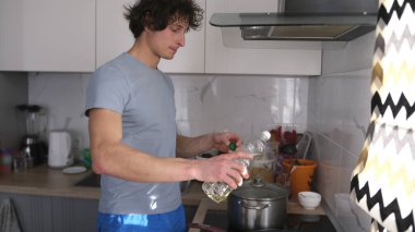 Yalnız bir beyaz adam mutfakta yemek pişirir, plastik bir şişeden tavaya sebze yağı döker. Şişe neredeyse boş. Mutfak iyi donatılmış: taş, lavabo.