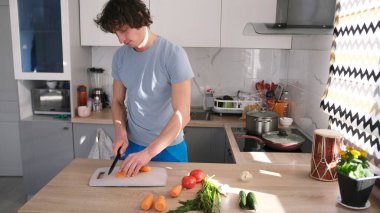 Avrupalı görünümlü yakışıklı bir adam eşcinsel arkadaşı için mutfakta akşam yemeği hazırlar. Kesme tahtasında havuç kesen bir adam. Sebzeler arasında sebze, domates ve salatalık vardır..