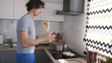 Yakışıklı bir bekar, elinde tahta bir kaşıkla mutfakta kızartma tavasında soğan kızartıyor. Mutfak iyi donatılmış. Adamın keyfi yerinde ve keyfi yerinde..