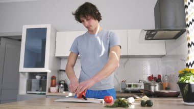 Seksi eşcinsel yakışıklı vejetaryen sebze salatasına domates kesiyor. Mutfak temiz ve iyi düzenlenmiş. Yakışıklı bir adam erkek arkadaşı için akşam yemeği pişirir..