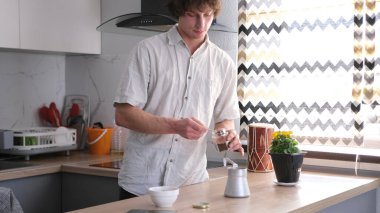 Taze kokulu kahve demleme sürecini izleyen bir adam. Yakışıklı genç bir adam bir Türk 'e kaşık dolusu kahve dolduruyor. Sabah rutinleri. Mutfak iyi donatılmış.