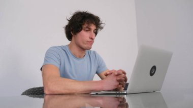 Genç, düşünceli bir adam dizüstü bilgisayarına bakıyor. Serbest çalışan bir bilgisayar üzerinde çalışıyor. Bir öğrenci önünde dizüstü bilgisayarla bir masada oturuyor. Mavi bir gömlek giyiyor ve işine odaklanmış..