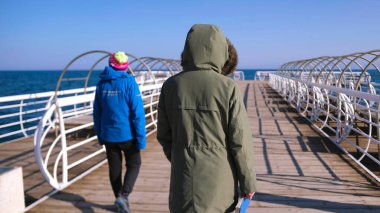 Kırgızistan 'daki Issyk-Kul Gölü boyunca yürüyen iki kız arkadaş. Orta Asya 'nın incisi. Arkadaşlar tahta kaldırım kullanıyor. Rıhtım boş, gökyüzü temiz.