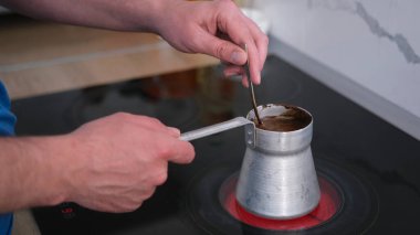Sıcak sobanın üstünde kahve karıştıran bir adamın yakın çekimi. Aromatik taze öğütülmüş kahve yapma süreci. Sabah ayini. Kahvaltı.
