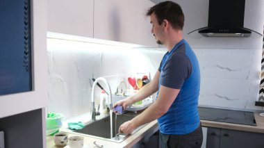 Genç bir adam mutfakta bulaşıkları yıkıyor. Adam mor bir sünger alır ve tabakları yıkar. Ev işleri işte. Yalnız bir öğrencinin hayatı.