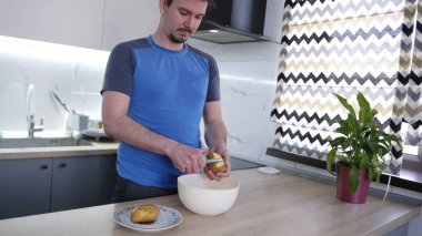 Sevimli bir eşcinsel erkek arkadaşı için lezzetli bir akşam yemeği pişirir. Adamın biri ahşap bir tezgahın üstünde patates soyarken. Mutfak modern bir şekilde ışıklandırılmış ve dekore edilmiş..