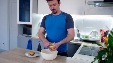 Kafkasyalı bir öğrenci ahşap bir tezgahta çiğ patates soyar. Lezzetli bir öğle yemeği pişiriyorum. Mutfakta mikrodalga fırın ve saksı bitkisi var..