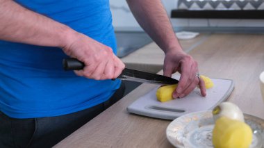 Genç bir öğrenci yakın plan kesim tahtasında çiğ patatesleri dilimliyor. Lezzetli bir öğle yemeği pişiriyorum. Kızarmış patates. Öğrenci hayatı. Mutfaktaki adam.