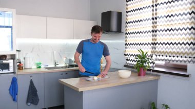 Kafkasyalı mutlu bir adam mutfak masasında sebze doğruyor. Şef akşam yemeği için lezzetli bir yemek hazırlıyor. Mutfak temiz ve iyi düzenlenmiş, mutfak masasının üzerinde saksı bitkisi ve yanında bir mikrodalga fırın var. Keyfi yerinde bir adam.