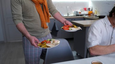 İki eşcinselin olduğu bir ailede sıradan bir akşam yemeği. Mutfak masasının önünde iki tabak lezzetli, ağız sulandırıcı yemek tutan bir adamın yakın çekimi. Kızarmış patates, yumurta ve taze sebze..
