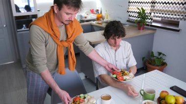 İki arkadaşın öğle yemeği. Önlerinde kızarmış yumurta ve taze sebzelerle dolu bir masada iki adam oturuyor. Sahne rahat.