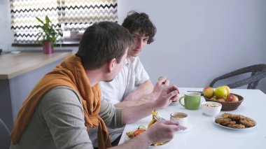 İki adam mutfakta otururken kahvaltıda sohbet ediyorlar. İki eşcinsel erkek arasında geçen bir konuşma. İki arkadaş şık bir mutfakta yemek yiyor.