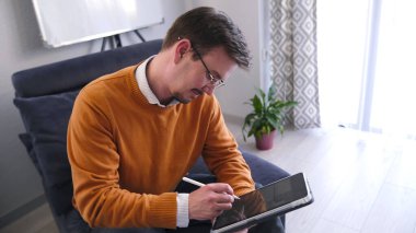 Turuncu kazaklı bir erkek öğretmen kanepede oturuyor ve tablete bir şeyler yazıyor. Röportaja hazırlanıyorum. Psikologun ofisi. Gözlük takıyor ve işine odaklanıyor. Odada bir saksı ve beyaz bir tahta var. 