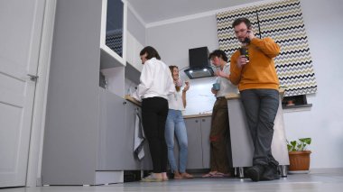 Bir grup ofis çalışanı mutfakta duruyor, bir tanesi cep telefonuyla konuşuyor. Sahne rahatladı, reklam ajansının meslektaşları kahve molası için toplandılar.