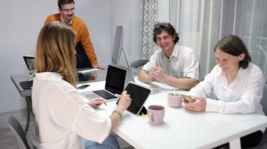 Beyin fırtınası. Meslektaşlar şaka yapar, güler ve güler. Bir grup ofis çalışanı dizüstü bilgisayarlı ve cep telefonlu bir masada oturuyor. Atmosfer dost canlısı ve rahat.