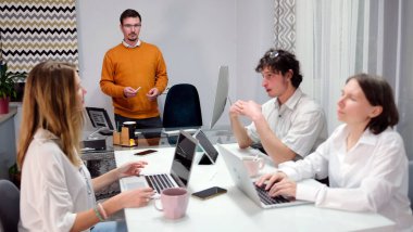 Bir psikolog, bir reklam ajansının küçük bir ofisinde kişisel gelişim eğitimi veriyor. Bir grup insan dizüstü bilgisayarlarla bir masada oturuyor ve bir adam sunum yapıyor. Sahne profesyonel ve odaklı.