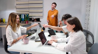 İş günü. Bir grup genç toplantı odasında dizüstü bilgisayarlarla beyaz bir ofis masasında oturuyor ve bir adam önlerinde duruyor ve onlara ne yapmaları gerektiğini söylüyor..