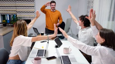 Anlaşmayı mutlu ve başarılı genç profesyonellerden oluşan bir ekip tamamladı. Bir grup insan konferans odasında birbirlerine beşlik çakıyor. Turuncu gömlekli adam grubun lideri.