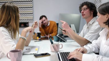 Yorgun bir patron yaratıcı ekibinin fikirlerini dinler. Birkaç kişi bir masada oturuyor ve bir projenin çalışmalarını tartışıyorlar. Masanın üzerinde birkaç dizüstü bilgisayar ve cep telefonu ve bardaklar var..