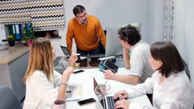 Şirket başkanı astlarından haftalık raporlarını isteyecektir. Ev ofisi. Bir grup insan konferans odasında bir masada oturuyor. Grup bir proje üzerinde çalışıyor ve ellerinde birkaç dizüstü bilgisayar var..