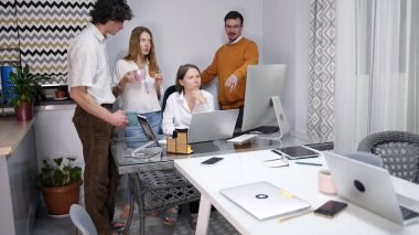 Bir grup iş arkadaşı dizüstü bilgisayar ekranında bir projeyi tartışıyor. Takım oluşturma ve beyin fırtınası. Bir grup insan dizüstü bilgisayarları ve cep telefonlarıyla bir masanın etrafında duruyorlar..