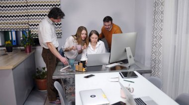 İki erkek ve iki kadın bir dizüstü bilgisayara bakıyor. Birkaç kişi iş kadınının masasının etrafında toplandı. Birlikte bir proje üzerinde çalışıyorlar..