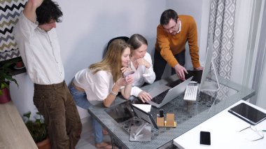 Genç pazarlama uzmanları için gayri resmi bir ofis. Bir grup insan dizüstü bilgisayarları ve kahve fincanlarıyla bir masada oturuyor ve ayakta duruyorlar. Birlikte bir proje üzerinde çalışıyorlar..