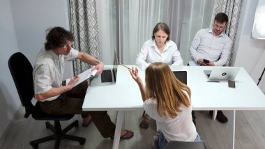 Patron yöneticiyle önemli belgeleri tartışıyor. Bir grup ofis çalışanı dizüstü bilgisayarlı ve cep telefonlu bir masada oturuyorlar. Projeyi tartışıyorlar.