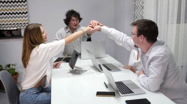 Başarılı takım ihaledeki zaferini kutluyor. Dizüstü bilgisayarların ve cep telefonlarının serildiği bir masanın önünde dört kişi el sıkışıyor. Sahne profesyonelce ve işbirliği ruhuyla gerçekleştirilir.