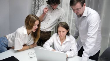 Meslektaşlar amirlerinin bilgisayar ekranına bakarlar. Bir grup insan yeni büyük bir proje üzerinde çalışıyor. Bir şey tartışıyorlar. Sahne işbirlikçi ve odaklı.