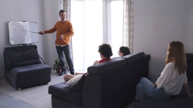 Bir erkek psikolog grup danışmanlığı yapıyor. Beyaz tahtanın önünde sunum konsepti. Arka planda, bir grup insan mavi koltuklarda oturuyor.