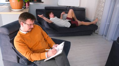 Turuncu kazaklı başarılı bir psikolog tablete bir şeyler yazarken genç bir adam kanepeye uzanıp sorunlarını anlatıyor. Bir adam genç bir adama tavsiye verir.