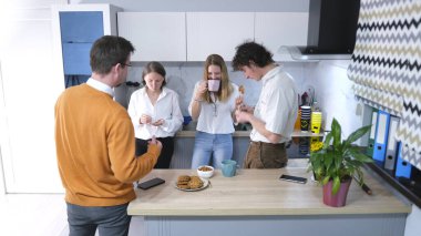 Kahve molası konsepti. Turuncu kazaklı bir adam iş arkadaşlarının yanında duruyor ve kahve içiyor. Hepsi kurabiye yer ve kahve içer..