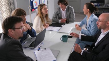 Bir grup genç iş adamı konferans odasındaki masada sohbet ediyorlar. Hepsi iş kıyafetleri giyip bir tartışma içindeler. Danışmanlık firması.