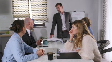 Şirket başkanı konferans odasında bir toplantı düzenliyor. Bir iş adamı sunum yapıyor. Atmosfer profesyonel ve odaklanmış görünüyor.