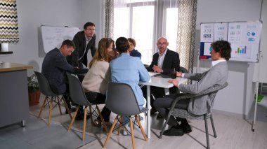 Şirketin başkanı sorunu nasıl çözeceğini düşünürken iki kadın birbirine fısıldıyor. Şirketin avukatına danışıyorum. Bir grup insan bir ofisteki masada oturuyor..