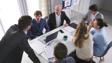 İş yeri konsepti. Müzakere masasında oturan insanların üst görüntüsü. Çalışanlar meslektaşlarının raporunu dinlerler. Bir projeyi tartışıyorlar..