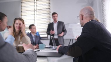 Diğerleri dinlerken adam bir sunum yapıyor. Bir psikolog ofiste verimliliği artırma ve takım çalışması üzerine bir ders veriyor. Sahne profesyonel ve odaklı.