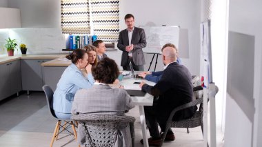 Adam bir sunum yapıyor ve grup derin bir tartışma içinde gibi görünüyor. Şirketin geliştirme stratejisinin tartışılması. İş yerinde bir toplantı..