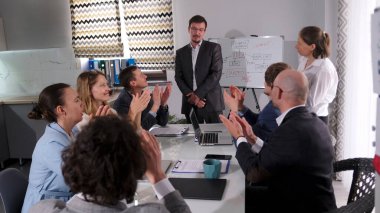 Başarılı bir profesyonel çalışan mütevazı bir şekilde meslektaşlarından tebrikleri kabul eder. Toplantıda birkaç kişi ellerini çırptı. Ortadaki adam duruyor ve bir sunum yapıyor.