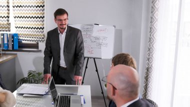 Cana yakın, yakışıklı bir iş danışmanı başarı stratejisi kavramından bahsediyor. Takım elbiseli bir adam üzerinde çizim olan beyaz bir tahtanın önünde duruyor..