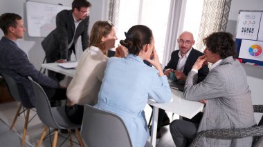 Çekici şirket çalışanları profesyonel sorumlulukları tartışıyor. Bir grup insan konferans odasında bir masada oturuyor. Takım elbiseli bir adam ayakta bir grupla konuşuyor..